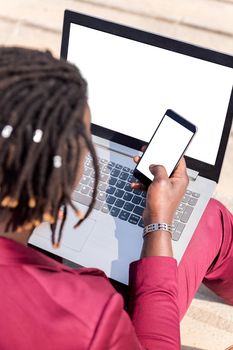 vertical photo of the rear view of an unrecognizable black businessman using a smart phone and computer laptop, technology and remote work concept, copy space for text