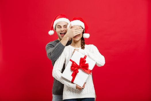 Christmas Concept - handsome young boyfriend in sweater surprise his girlfriend with white gift.