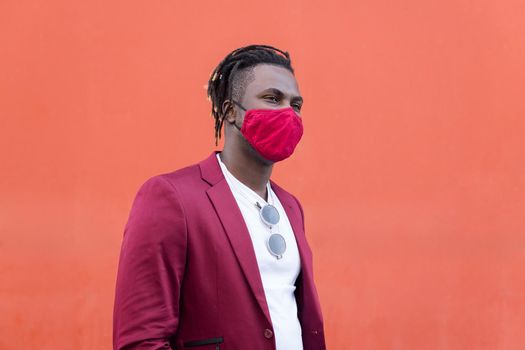 stylish black man with protective mask to match his suit on a red background, concept of elegance and fashionable lifestyle, copy space for text