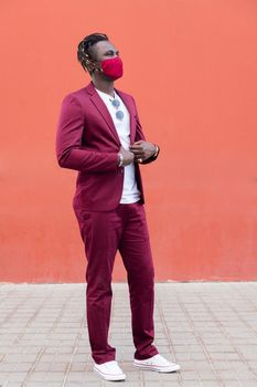 vertical photo of a handsome black man with protective mask to match his suit on a red background, concept of elegance and fashionable lifestyle