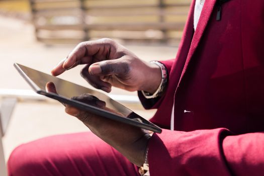 detail of the hands of an african man using a tablet outdoors in the city, technology and remote work concept