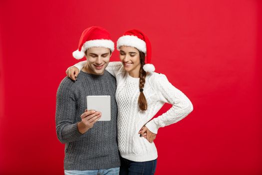 Christmas Concept - Young handsome and beautiful couple enjoy playing on tablet in christmas day.