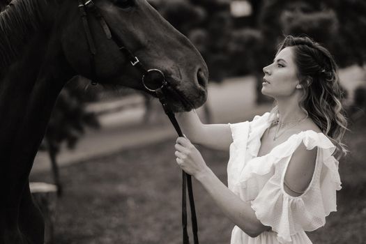 Beautiful girl in a white sundress next to a horse on an old ranch. black and white photo.