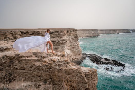 Happy freedom woman on the beach enjoying and posing in white dress over the sea. View of a girl in a fluttering white dress in the wind. Holidays, holidays at sea