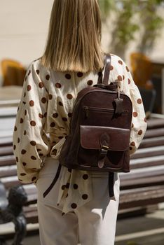 Woman with a brown leather backpack with antique and retro look. Outdoors photo.