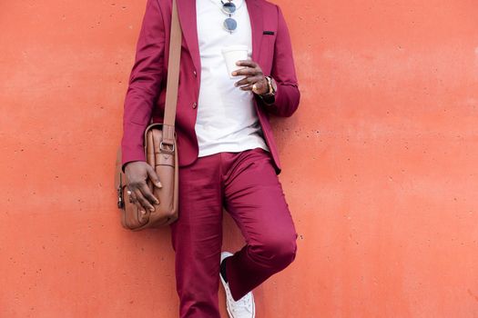 unrecognizable elegant african businessman dressed in suit with briefcase holding coffee in his hand in front of red background, copy space for text