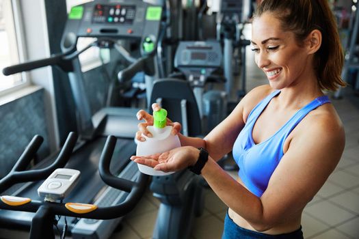 Young woman cleaning hands with liquid soap in front of fitness gym equipment