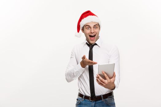 Christmas Concept - Handsome Business man wear santa hat playing tablet with surprising facial expression.