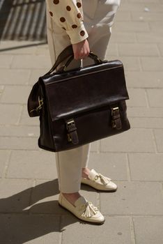 Woman with a brown leather briefcase with antique and retro look. Outdoors photo.