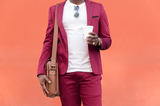 unrecognizable elegant black businessman dressed in suit with briefcase holds coffee in his hand in front of red background, copy space for text