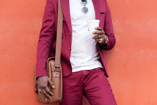 unrecognizable stylish african businessman dressed in suit with briefcase holding coffee in his hand in front of red background, copy space for text