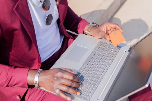 detail of the hands of a black man paying with his credit card for the online purchase made with his laptop computer, concept of technology and online shopping