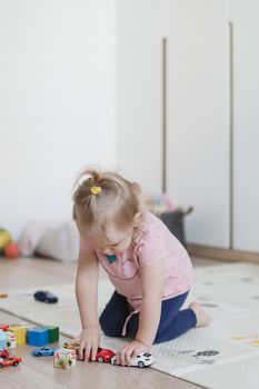 a little funny girl plays with cubes and toys on the floor in the nursery.