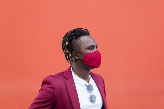 elegant black man with protective mask to match his suit on a red background, concept of elegance and fashionable lifestyle, copy space for text