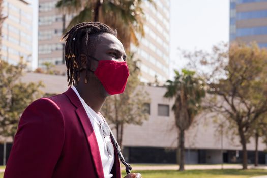 portrait of a black businessman walking around the city with a red mask to match his suit, concept of elegance and fashionable lifestyle, copy space for text