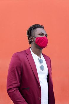vertical photo of a stylish black man with protective mask to match his suit on a red background, concept of elegance and fashionable lifestyle, copy space for text