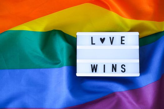 Rainbow flag with lightbox and text LOVE WINS. Rainbow lgbtq flag made from silk material. Symbol of LGBTQ pride month. Equal rights. Peace and freedom. Support LGBTQ community