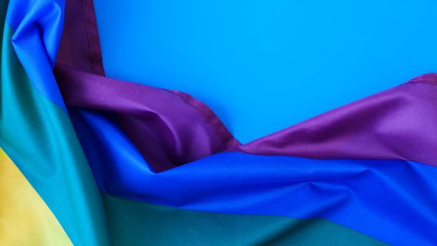Rainbow flag on blue background with copy space. Rainbow lgbtq flag made from silk material. Symbol of LGBTQ pride month. Equal rights. Peace and freedom. Support LGBTQ community