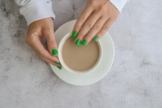 Manicured female hands with stylish green nails holding cup of coffee. Take a break for coffee latte. Trendy modern design manicure. Gel nails. Skin care. Beauty. Nail care. Wellness