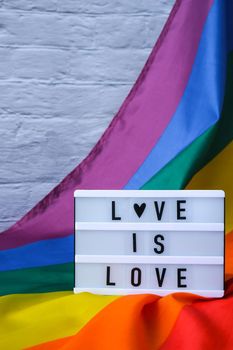 Rainbow flag with lightbox and text LOVE IS LOVE. Rainbow lgbtq flag made from silk material. Symbol of LGBTQ pride month. Equal rights. Peace and freedom. Support LGBTQ community
