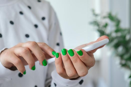 Manicured female hands with stylish green nails holding mobile phone. Smartphone technology. Trendy modern design manicure. Gel nails. Skin care. Beauty treatment. Nail care. Wellness. Trendy colors.