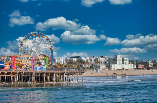 Picturesque cityscape of coastal Santa Monica city with sandy beach and colorful Ferris wheel, near sea under blue cloudy sky, in summer day in California USA