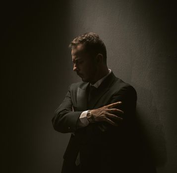 Pensive businessman stands against dark background. Thinking middle-aged man thoughtfully hugged himself with his hands against the wall. depression concept. bankruptcy concept. Toned image.