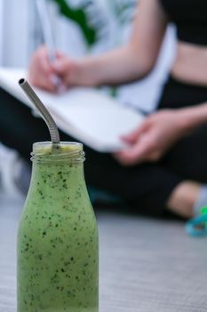 Seasonal Matcha green vegan smoothie with chia seeds and mint smoothie drink detox. Woman writing results and goals on background Clean eating, weight loss, healthy dieting food concept. Fitness training workout at home.