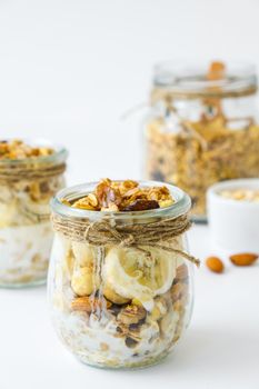 Healthy breakfast. Oatmeal Granola with greek yogurt and nuts banana muesli in jars on light background. Vegan, vegetarian and weight loss diet concept. Detox menu. Healthy eating food