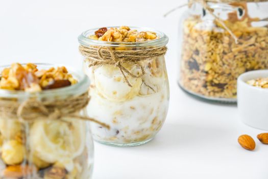 Healthy breakfast. Oatmeal Granola with greek yogurt and nuts banana muesli in jars on light background. Vegan, vegetarian and weight loss diet concept. Detox menu. Healthy eating food