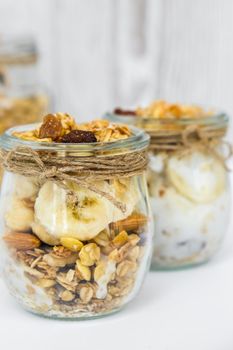 Healthy breakfast. Oatmeal Granola with greek yogurt and nuts banana muesli in jars on light background. Vegan, vegetarian and weight loss diet concept. Detox menu. Healthy eating food