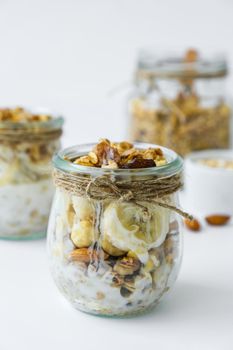 Healthy breakfast. Oatmeal Granola with greek yogurt and nuts banana muesli in jars on light background. Vegan, vegetarian and weight loss diet concept. Detox menu. Healthy eating food