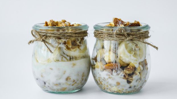 Healthy breakfast. Oatmeal Granola with greek yogurt and nuts banana muesli in jars on light background. Vegan, vegetarian and weight loss diet concept. Detox menu. Healthy eating food