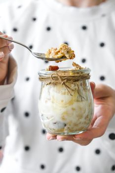 Female hands, woman eating Healthy breakfast. Oatmeal Granola with greek yogurt and nuts banana muesli in jars on light background. Vegan, vegetarian and weight loss diet concept. Detox menu. Healthy eating food