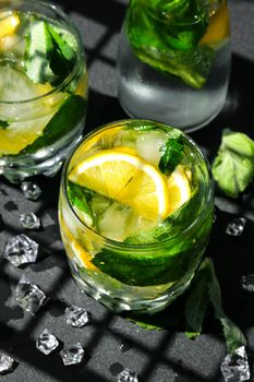 Mojito refreshing cocktail, alcohol drink. Lemonade with lemon and mint leaves on dark background. Trendy shadows Ice cubes. Summer refreshing detox drinks. Clean eating, healthy lifestyle concept, Diet. Nutrition