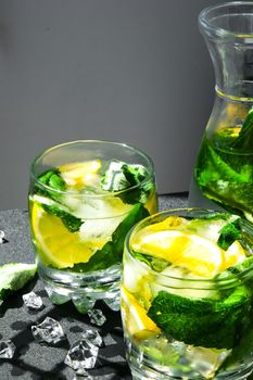 Mojito refreshing cocktail, alcohol drink. Lemonade with lemon and mint leaves on dark background. Trendy shadows Ice cubes. Summer refreshing detox drinks. Clean eating, healthy lifestyle concept, Diet. Nutrition