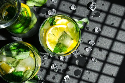 Mojito refreshing cocktail, alcohol drink. Lemonade with lemon and mint leaves on dark background. Trendy shadows Ice cubes. Summer refreshing detox drinks. Clean eating, healthy lifestyle concept, Diet. Nutrition. Top view