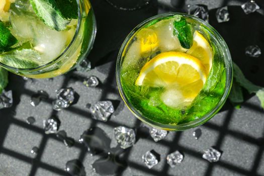 Mojito refreshing cocktail, alcohol drink. Lemonade with lemon and mint leaves on dark background. Trendy shadows Ice cubes. Summer refreshing detox drinks. Clean eating, healthy lifestyle concept, Diet. Nutrition. Top view