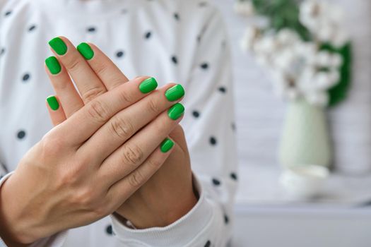 Manicured female hands with stylish green nails. Trendy modern design manicure. Gel nails. Skin care. Beauty treatment. Nail care. Wellness. Trendy colors.