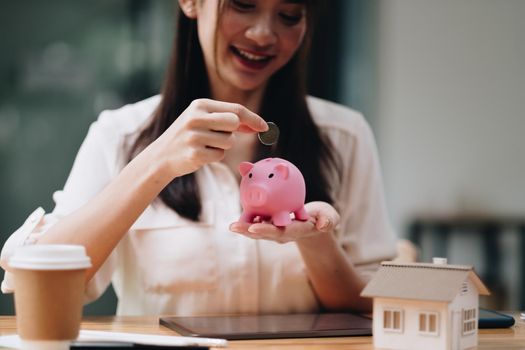 mortgage, investment, real estate and property concept - close up of woman putting money into pink piggy bank for loan or save for buy a new house.