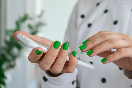 Manicured female hands with stylish green nails holding mobile phone. Smartphone technology. Trendy modern design manicure. Gel nails. Skin care. Beauty treatment. Nail care. Wellness. Trendy colors.