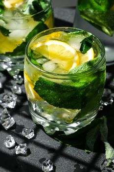 Mojito refreshing cocktail, alcohol drink. Lemonade with lemon and mint leaves on dark background. Trendy shadows Ice cubes. Summer refreshing detox drinks. Clean eating, healthy lifestyle concept, Diet. Nutrition