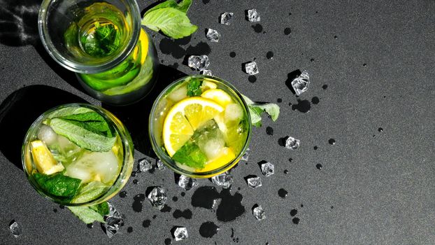 Mojito refreshing cocktail, alcohol drink. Lemonade with lemon and mint leaves on dark background. Ice cubes. Summer refreshing detox drinks. Clean eating, healthy lifestyle concept, Diet. Nutrition. Top view