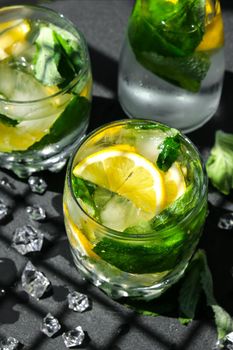 Mojito refreshing cocktail, alcohol drink. Lemonade with lemon and mint leaves on dark background. Trendy shadows Ice cubes. Summer refreshing detox drinks. Clean eating, healthy lifestyle concept, Diet. Nutrition