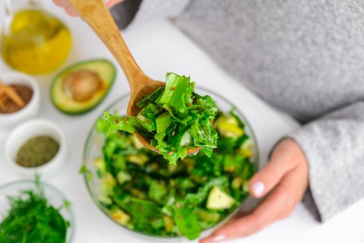 Woman mix salad of fresh green vegetables and herbs. Cooking healthy diet or vegetarian food. Step by step recipe. Healthy eating. Ingredients for salad. Pattern flat lay with healthy vegetarian meal ingredients. Raw food concept. A variety of organic fruits and vegetables with avocado. Vegan menu. Fresh spinach and green onion leaves, arugula.