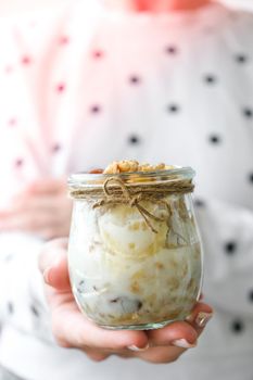 Female hands, woman eating Healthy breakfast. Oatmeal Granola with greek yogurt and nuts banana muesli in jars on light background. Vegan, vegetarian and weight loss diet concept. Detox menu. Healthy eating food