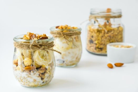 Healthy breakfast. Oatmeal Granola with greek yogurt and nuts banana muesli in jars on light background. Vegan, vegetarian and weight loss diet concept. Detox menu. Healthy eating food