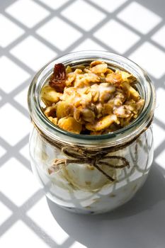 Healthy breakfast. Oatmeal Granola with greek yogurt and nuts banana muesli in jars on light background. Trendy shadows Vegan, vegetarian and weight loss diet concept. Detox menu. Healthy eating food