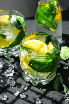 Mojito refreshing cocktail, alcohol drink. Lemonade with lemon and mint leaves on dark background. Trendy shadows Ice cubes. Summer refreshing detox drinks. Clean eating, healthy lifestyle concept, Diet. Nutrition