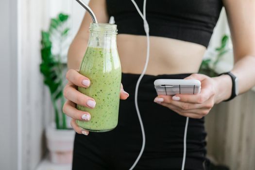 Young millenial woman checking smartphone drinking vegan smoothie drink detox. Woman doing yoga exercises at home. Online tuition Clean eating, weight loss, healthy dieting food concept. Stay healthy. Wellness